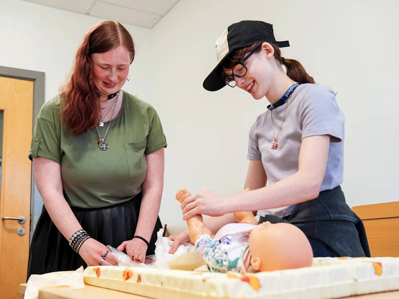 Two happy early years students training with baby mannequin